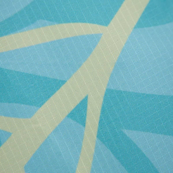 A square outdoor blanket in aqua and light cream with a textured geometric pattern, featuring a logo.