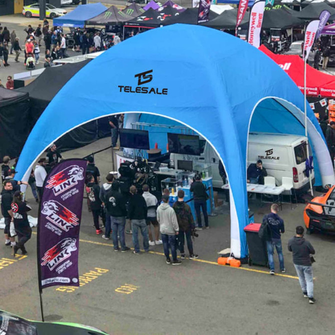 A blue inflatable marquee with a logo, set up in a busy event area, surrounded by people and banners.