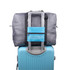A grey travel compressed bag attached to the handle of a blue suitcase. The bag features a pocket and a logo.