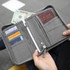 A grey passport holder with compartments for cards, cash, and a boarding pass, held open by a person.