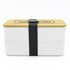 A two-layer lunch box in white with a bamboo lid, secured by a black strap. It features a logo on the top.