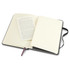 A black Moleskine Classic Hard Cover Notebook opened to reveal blank pages and a small folded leaflet inside.