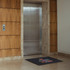 A nylon floor mat in front of a sleek elevator, featuring a logo and multicoloured text on a dark background.
