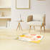 A plush logo mat featuring colourful floral designs, placed on a wooden floor next to a minimalist chair and table.