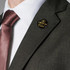 A lapel pin displayed on a dark green jacket, featuring a circular design with a gold logo.