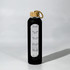 A drink bottle in black glass with a wooden lid and a rope handle, featuring measurement markings on the side.
