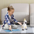 A child with a plaid shirt sits on a rug, holding a game board, next to a white and yellow cockatoo plush toy.