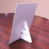 A white promotional counter card stands upright on a wooden table, featuring a simple triangular support at the back.