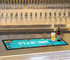 A bar runner in vibrant teal featuring tropical designs, placed on a polished bar with drinks nearby.