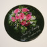 A round coaster featuring a bouquet of pink roses with green accents, adorned with text and a logo.