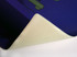 A purple mouse mat with a textured surface, featuring a white, rolled edge. It has a logo visible in the design.