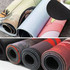 Rolled gaming mats in various colours, featuring textured surfaces and a smooth underside, alongside others with a black finish.