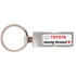 A metal keyring with a silver finish features a rectangular design and a logo. It has a circular keyring attachment.