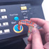 A transparent tool with an orange design, being used to press a button on a machine. It has a logo.