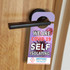 A door hanger in vibrant colours featuring a logo, designed to indicate self-isolation due to COVID-19.