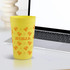 A yellow plastic stadium cup with an orange design and a logo, placed next to a laptop on a desk.