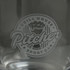 A glass pitcher featuring an etched logo, showcasing a classic design in transparent glass.