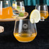 A wine glass filled with orange liquid, garnished with a slice of lemon, with additional glasses in the background.