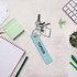 A light blue woven key tag attached to keys, surrounded by stationery and a small plant.