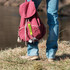 A keyring in yellow attached to a maroon backpack, held by a person standing on grass near a riverbank.