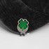 A green and gold soft enamel golf ball marker featuring a four-leaf clover design, resting on a black cap.