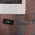 A black capsule storage charging cable with three connectors rests next to a silver laptop on a wooden surface.