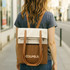 A woman walks down the street carrying a convertible canvas backpack in cream and brown with shoulder straps.