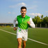 A man is running on a sports field, wearing a green and white long-sleeve polo with a logo.