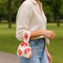 A wrist bag featuring a pink strawberry design, held by a person wearing a light-coloured shirt and jeans.