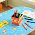 A four-panel foldable pen holder in red, yellow, and black, filled with vibrant pens and sitting on a playful tablecloth.