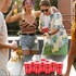 A set of red party cups arranged for beer pong, with people enjoying drinks and playing in a lively outdoor setting.