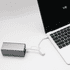 A silver power bank connected to a laptop via a white charging cable. The laptop screen shows a battery charge indicator.