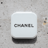 A compact mirror in a white case with a logo on the top, set against a textured stone background.