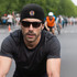A black cycling bandana hat worn by a man with sunglasses, set against a blurred outdoor cycling scene.