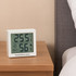 A white digital thermometer displays temperature at 25.5°C and humidity at 56%, placed on a wooden bedside table.