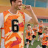 A vibrant orange training bib with a number and abstract design, worn by a man, with children running in the background.