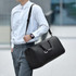A black polyurethane duffle bag with handles and a shoulder strap, carried by a person in formal attire.