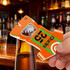 A drink bottle opener keyring shaped like a sport jersey in orange with green stripes and a logo.