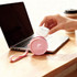 A round pink silicone coin pouch with a strap sits on a desk beside a laptop and a coffee cup.