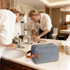 A grey toiletry bag with a brown leather handle is placed on a bathroom countertop next to a sink.