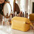 A large yellow PU toiletry bag sits on a marble surface near skincare products and a mirror.
