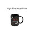 A black mug featuring a decorative design with cranes and floral elements. It has a brand logo.