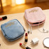 A pink and blue stylish mini makeup bag with golden branding, surrounded by lipsticks, earbuds, and a charger.