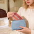 A blue flat makeup bag with a gold zipper is being held, with a cosmetics palette being placed inside.