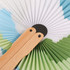A wooden paper fan featuring a peach shape design with green and blue patterns. The fan has wooden handles.