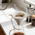 A stainless steel coffee filter in a conical shape, with water being poured through it into a glass jug.