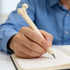 A hand holding a cream-coloured pen shaped like a femur bone, poised above an open notebook.