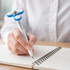 A blue and white fidget pen with a spinning topper, held above an open notebook. The pen features a logo.