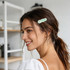 A hair clip in an iridescent alligator style, featuring shades of green, worn by a smiling woman with long hair.