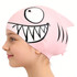 A pink silicone swim cap with a fish design, featuring a large smiling face and fins, shown on a child's head.
